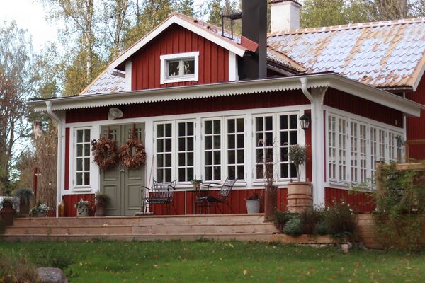 Rött trähus med stor spröjsad glasveranda i trä