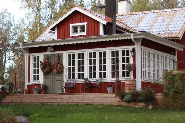 Rött trähus med stor spröjsad glasveranda i trä