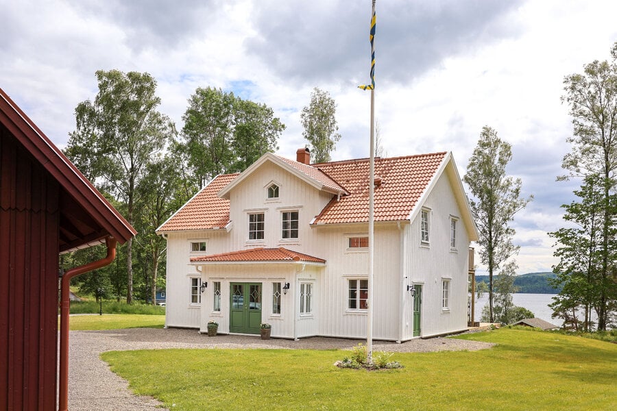 Vitt panelhus med tegeltak, spröjsade träfönster och grön pardörr i modell Sekel