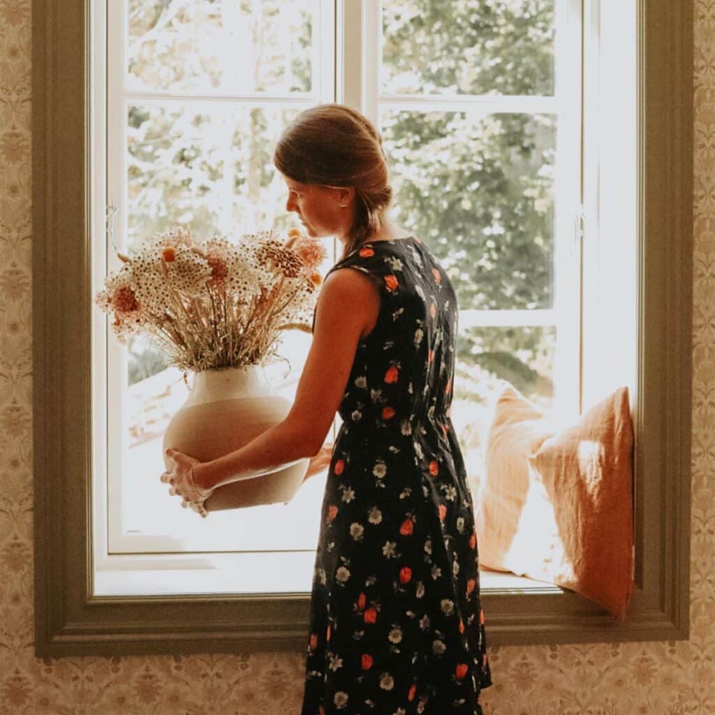 Kvinna ställer blomma vid fönster